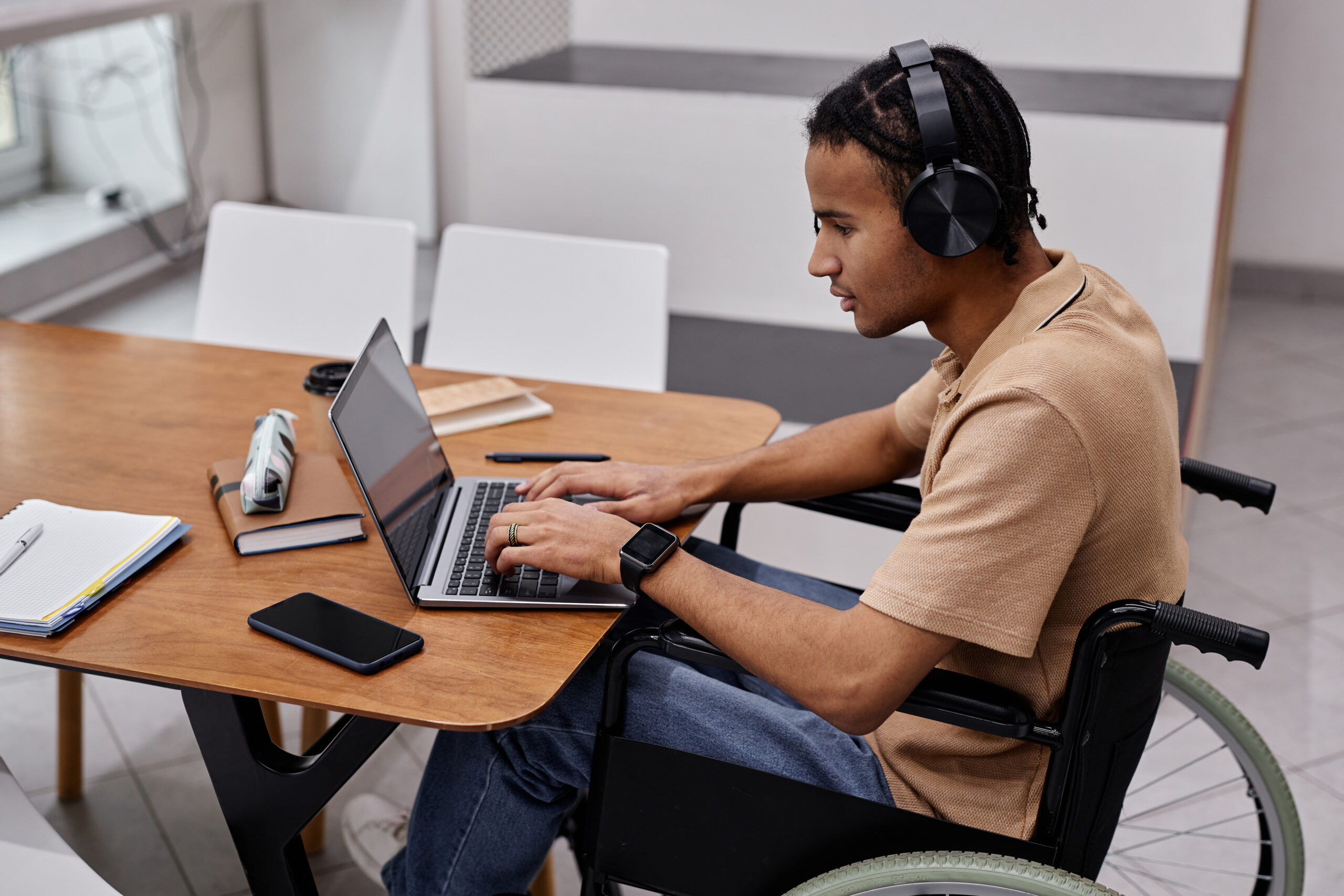 A young man with disability using laptop in a library and wearing headphones